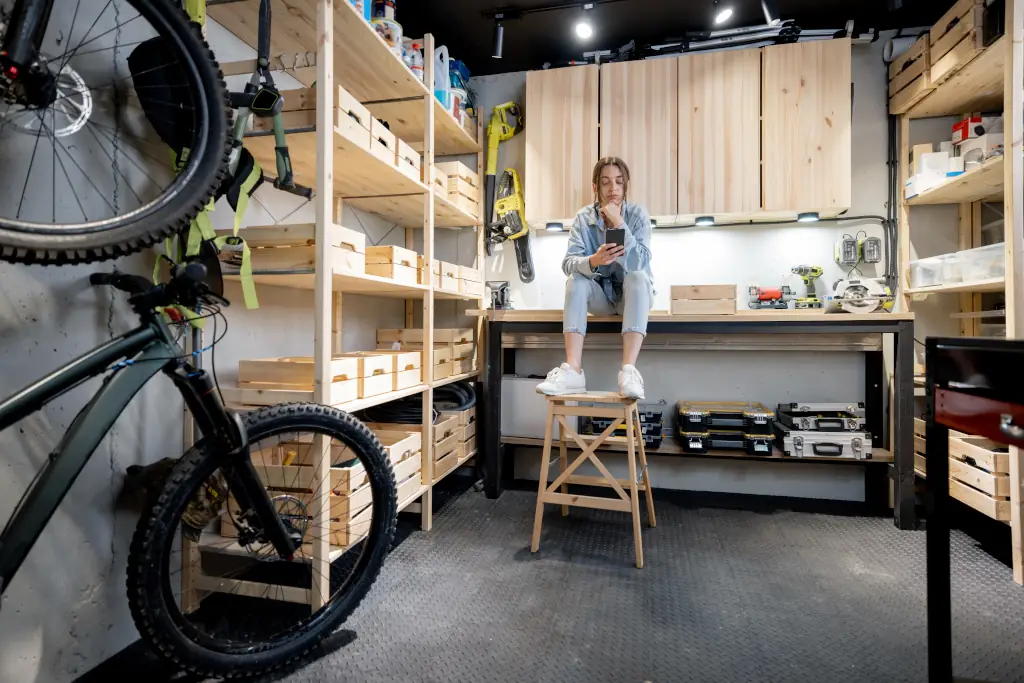 A garage with organized boxes, tools, and furniture and a young woman